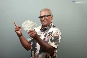 A man in glasses holds up money and points, suggesting the opportunity to make money with online surveys.