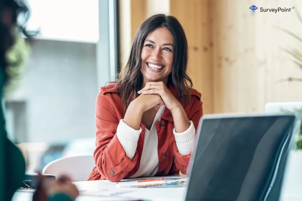 A woman happily sitting at a table with a laptop, participating in an online survey.