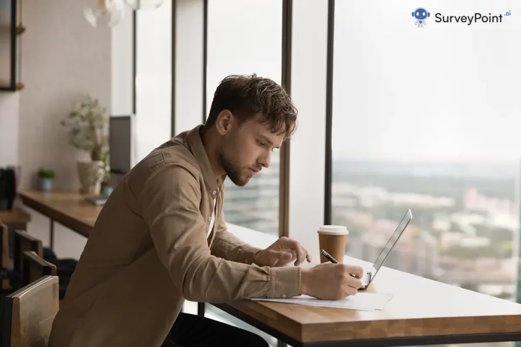 A man sitting at a table with a laptop and coffee, participating in the Clarity Research Survey.