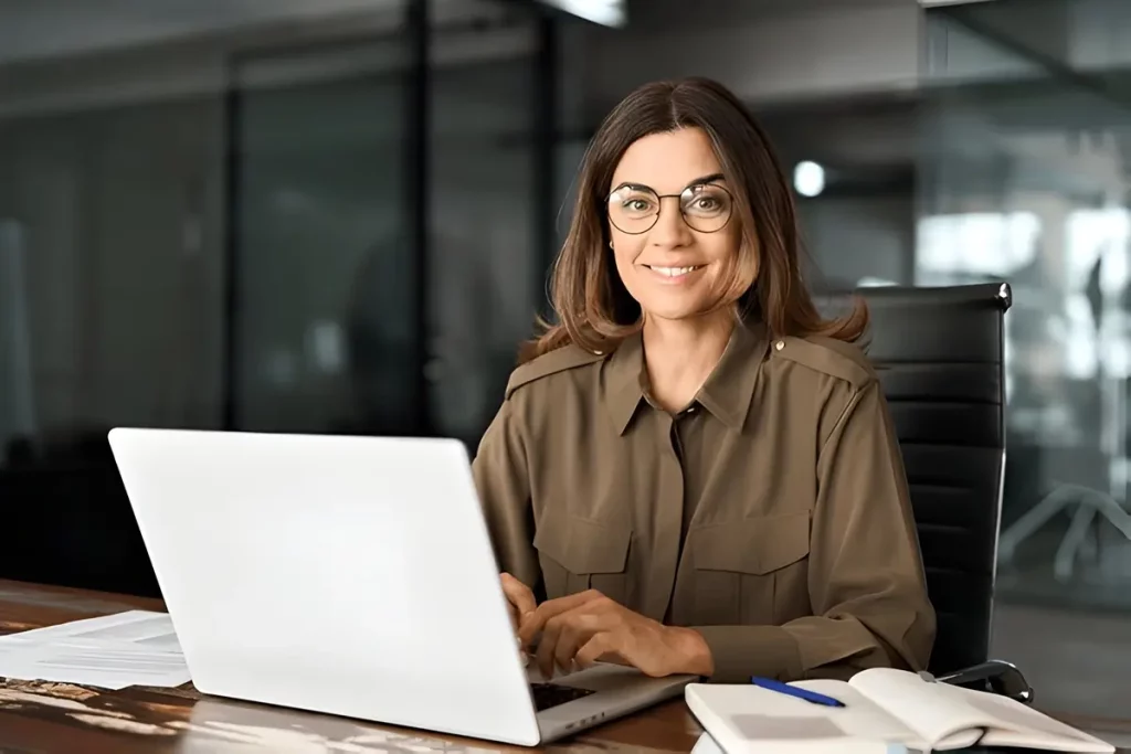 A woman wearing glasses sits at a desk, focused on her laptop, preparing to analyze food truck survey questions.