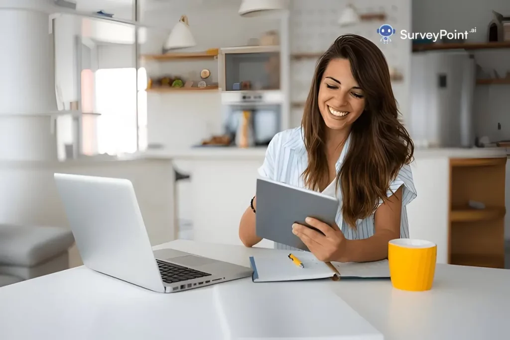 A woman sitting at a table with a laptop and tablet, working on SEL Survey Questions.