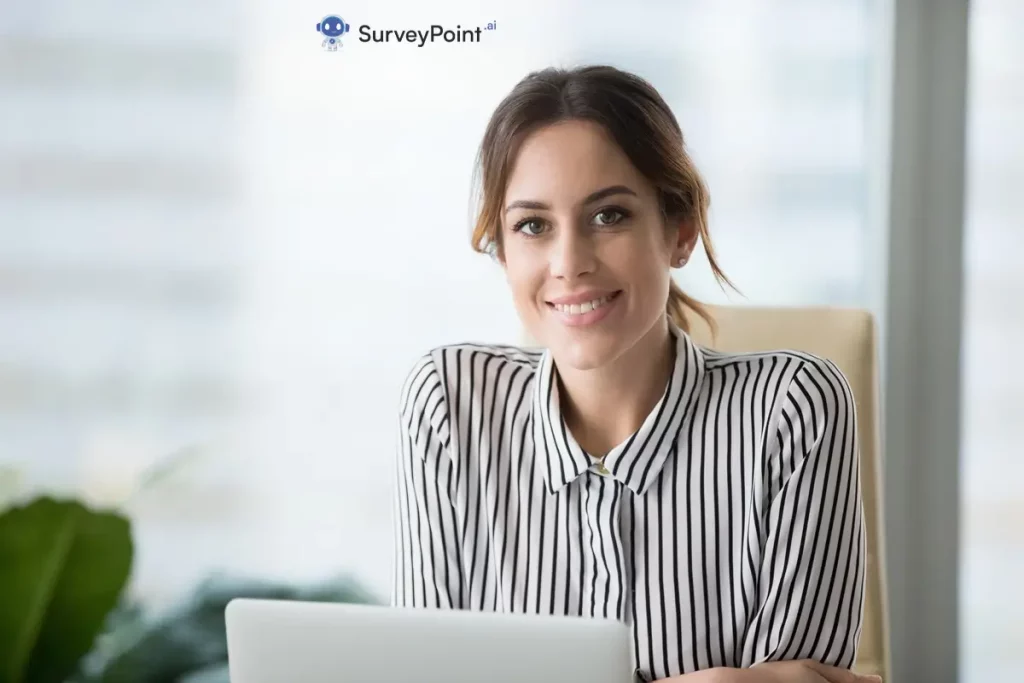 A woman in a striped shirt smiles while using a laptop, engaged in a Belonging Survey Questions session.