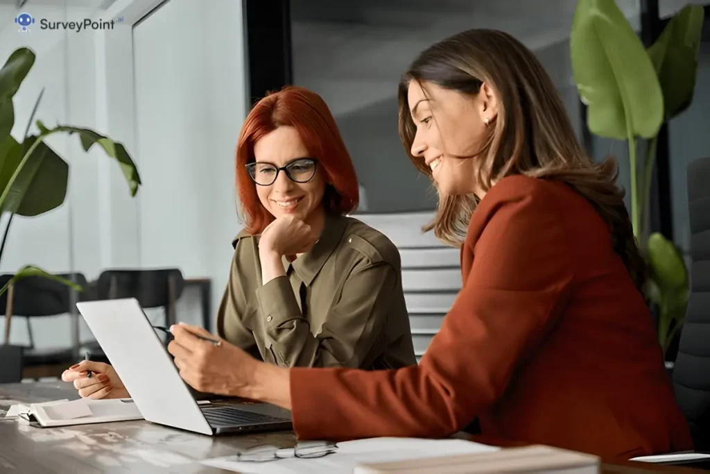 Two women engaged in discussion at a table, working collaboratively on a laptop for the Glint Survey project.