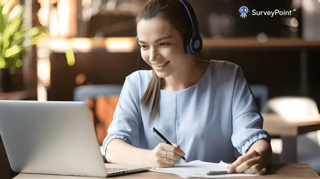 A woman wearing headphones sits at a table, focused on her laptop, engaged in a reading survey for elementary students.