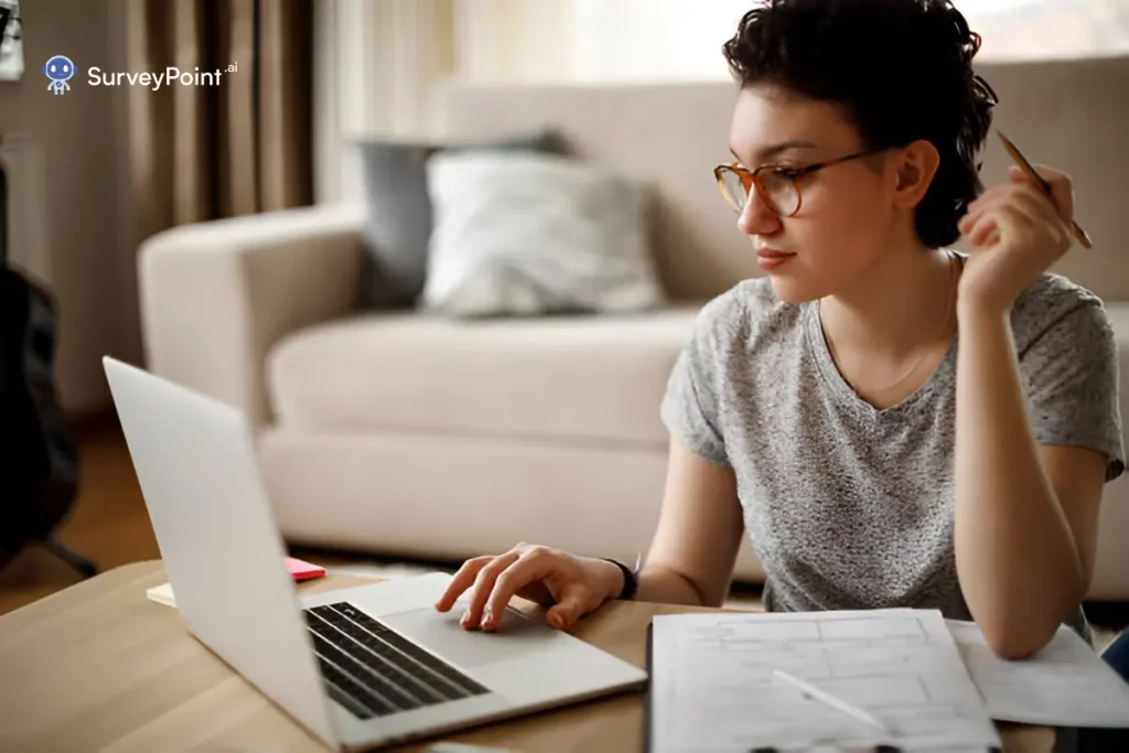 A woman in glasses is at a table, using her laptop, possibly to answer pre training survey questions.