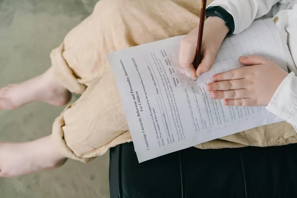 A person seated on a chair, writing notes with a pen on paper, reflecting on employee motivation survey.