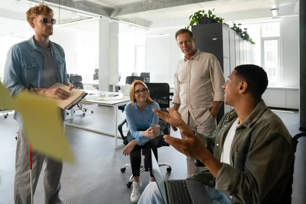 A diverse group of individuals engaged in discussion within an office setting, focusing on inclusion survey questions.