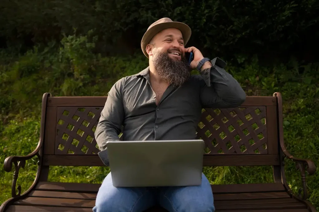 A bearded man on a bench uses a laptop, with hilarious surveyor jokes displayed around him.