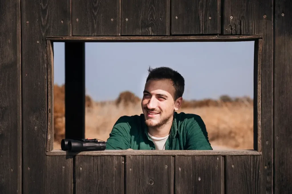 A man gazes thoughtfully out a window of a rustic wooden building, contemplating the humor in surveying.