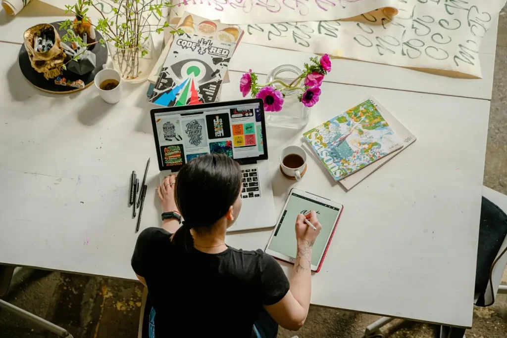 A woman at a table uses a laptop and pen, focused on creating a workshop survey questionnaire to gather valuable feedback.